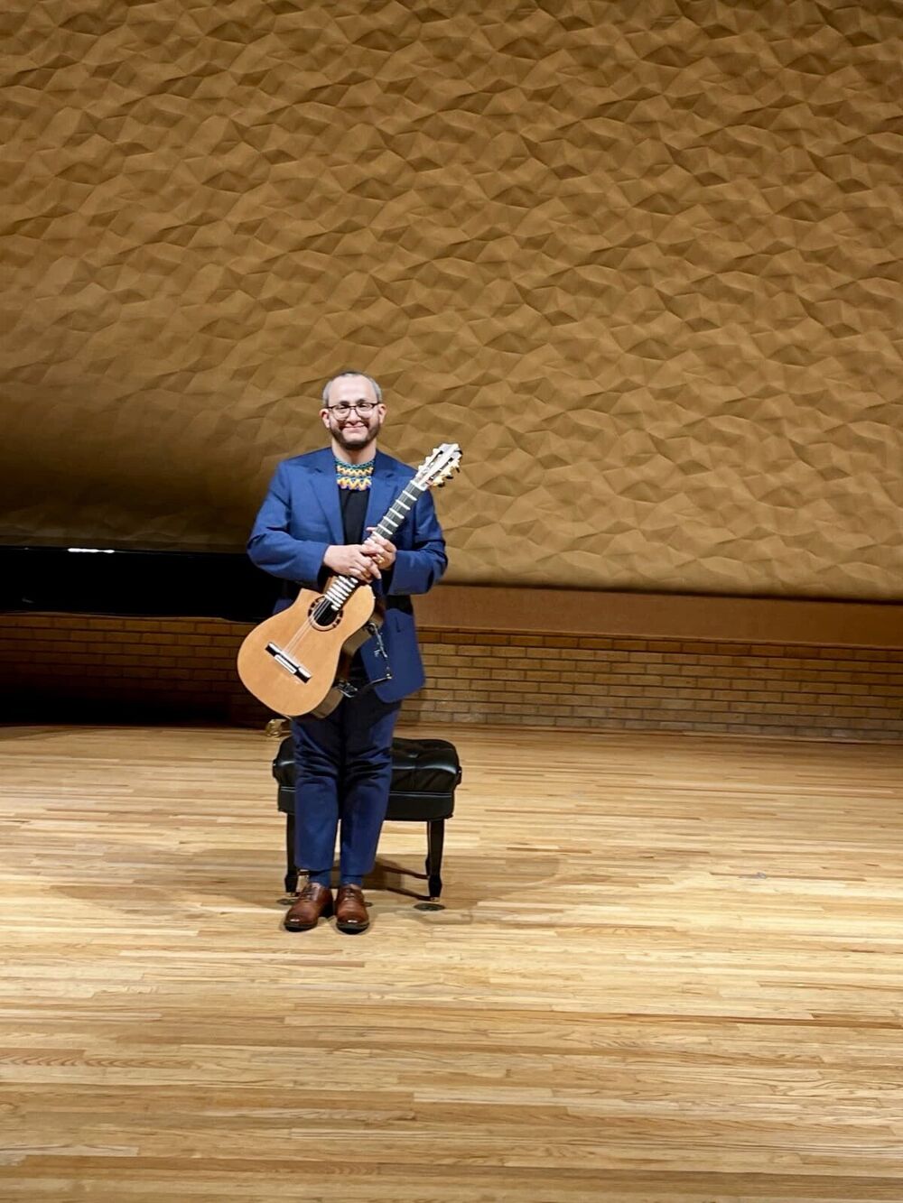 Andrés David Arcila standing with his classical guitar in a concert hall